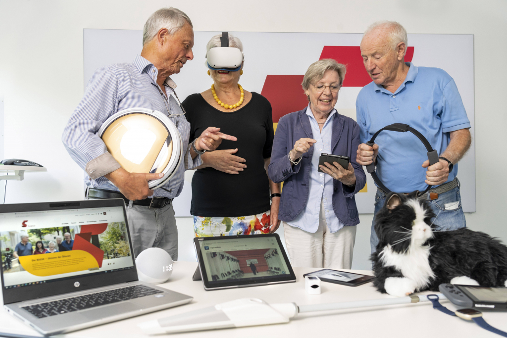 Vier ältere Menschen testen verschiedene digitale Geräte