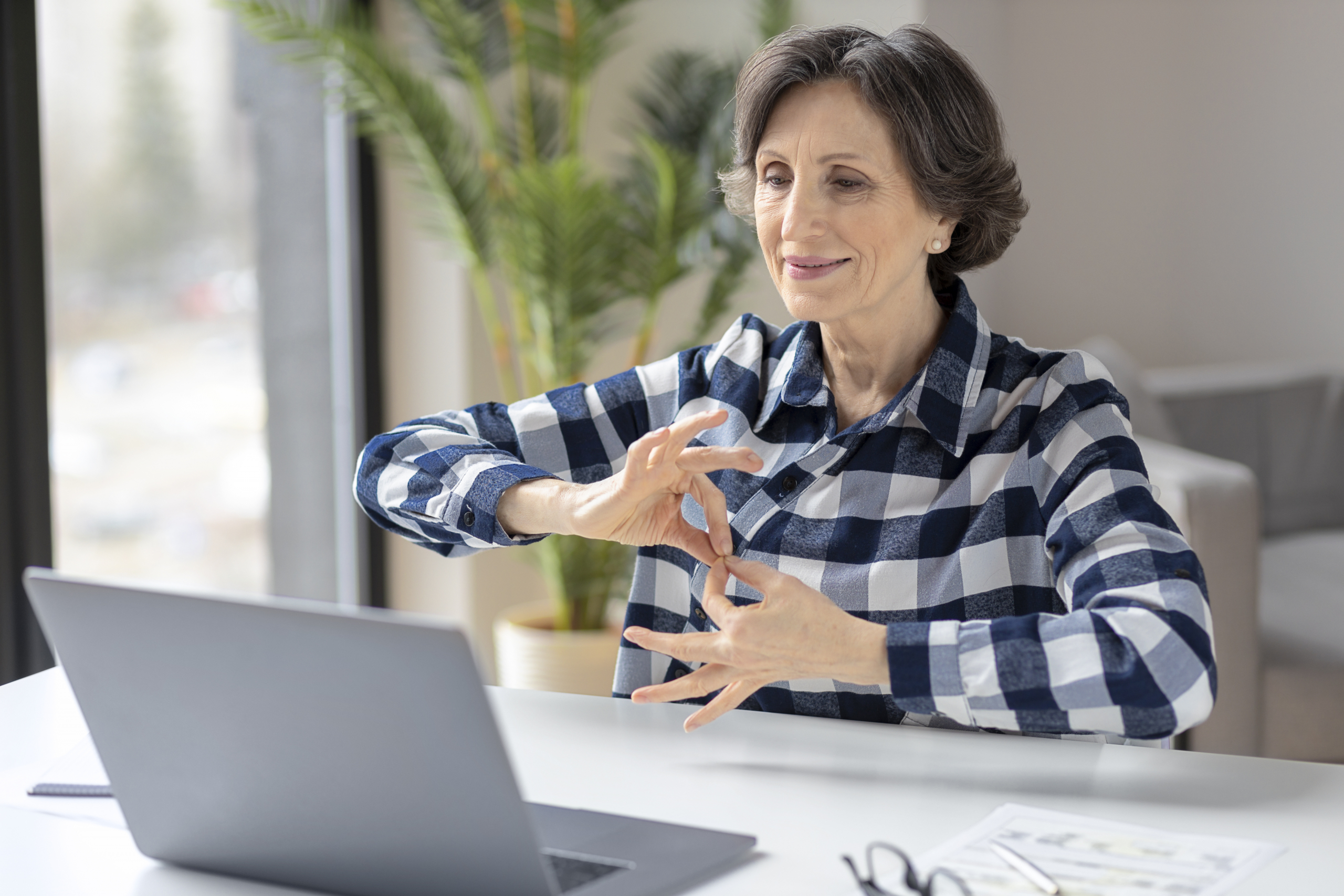 Deaf elderly woman uses sign language while video call using laptop while sitting in home office