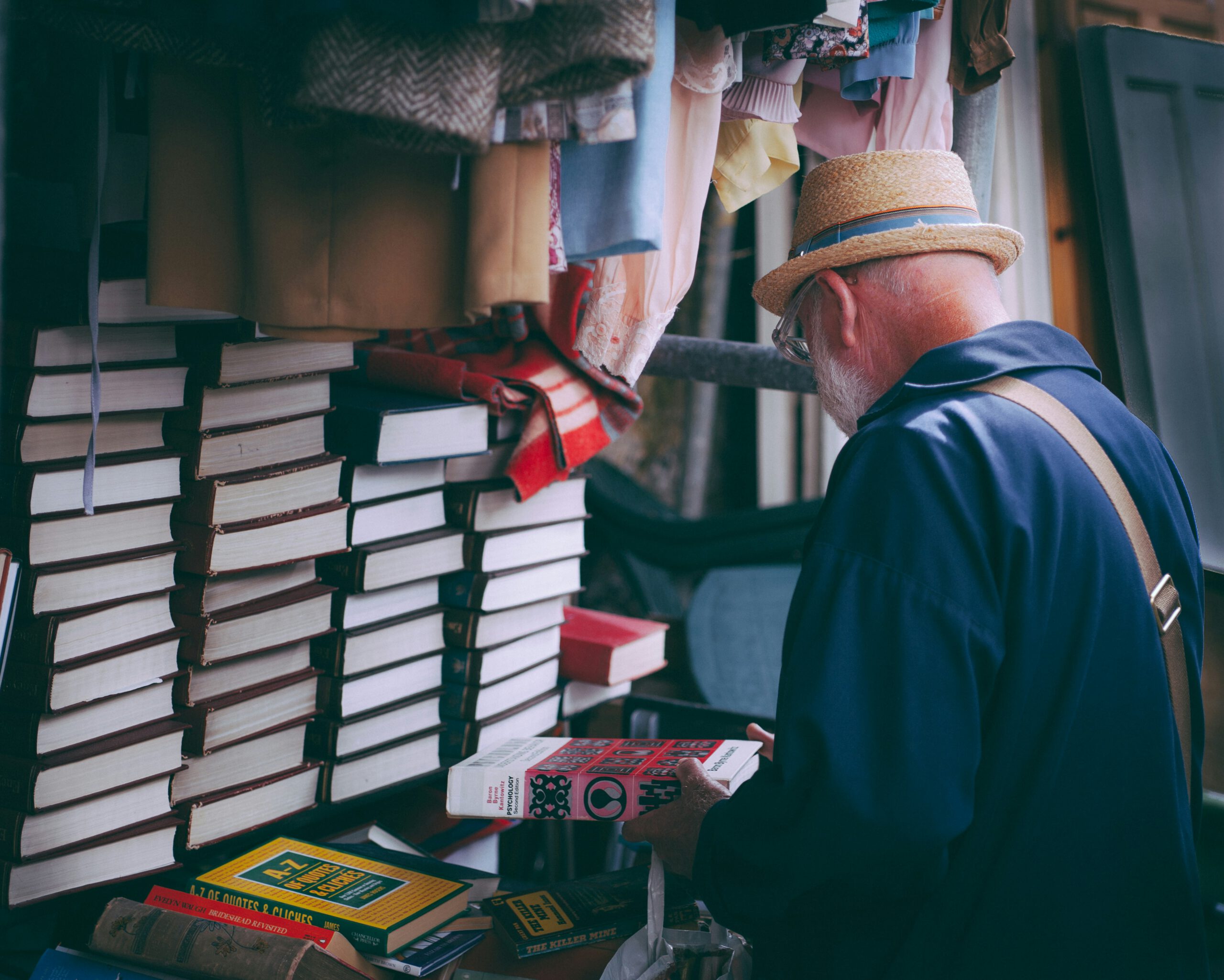 Ein älterer Herr mit Hut schaut sich einen Stapel Bücher an.